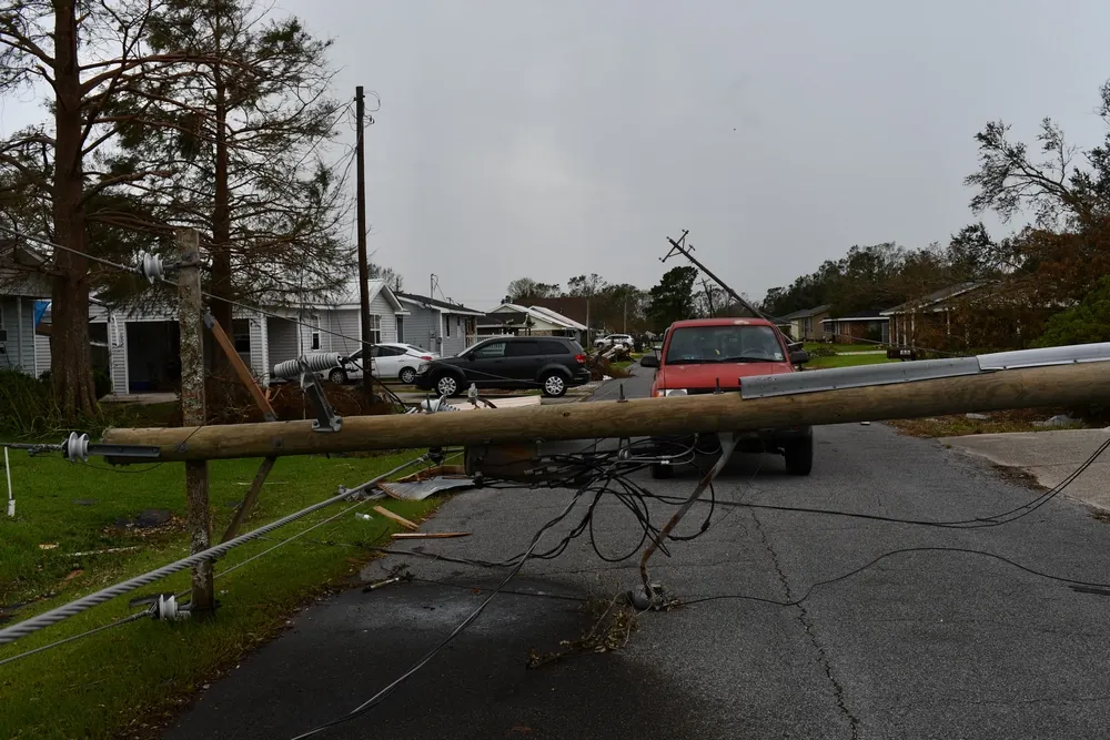 Downed utility pole and power lines blocking a residential street after a hurricane