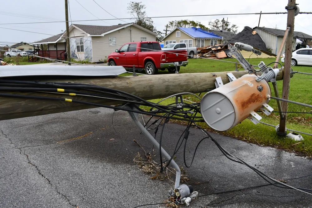 Downed power pole and wires in a Louisiana neighborhood after Hurricane Ida, with a blue-tarp roof behind