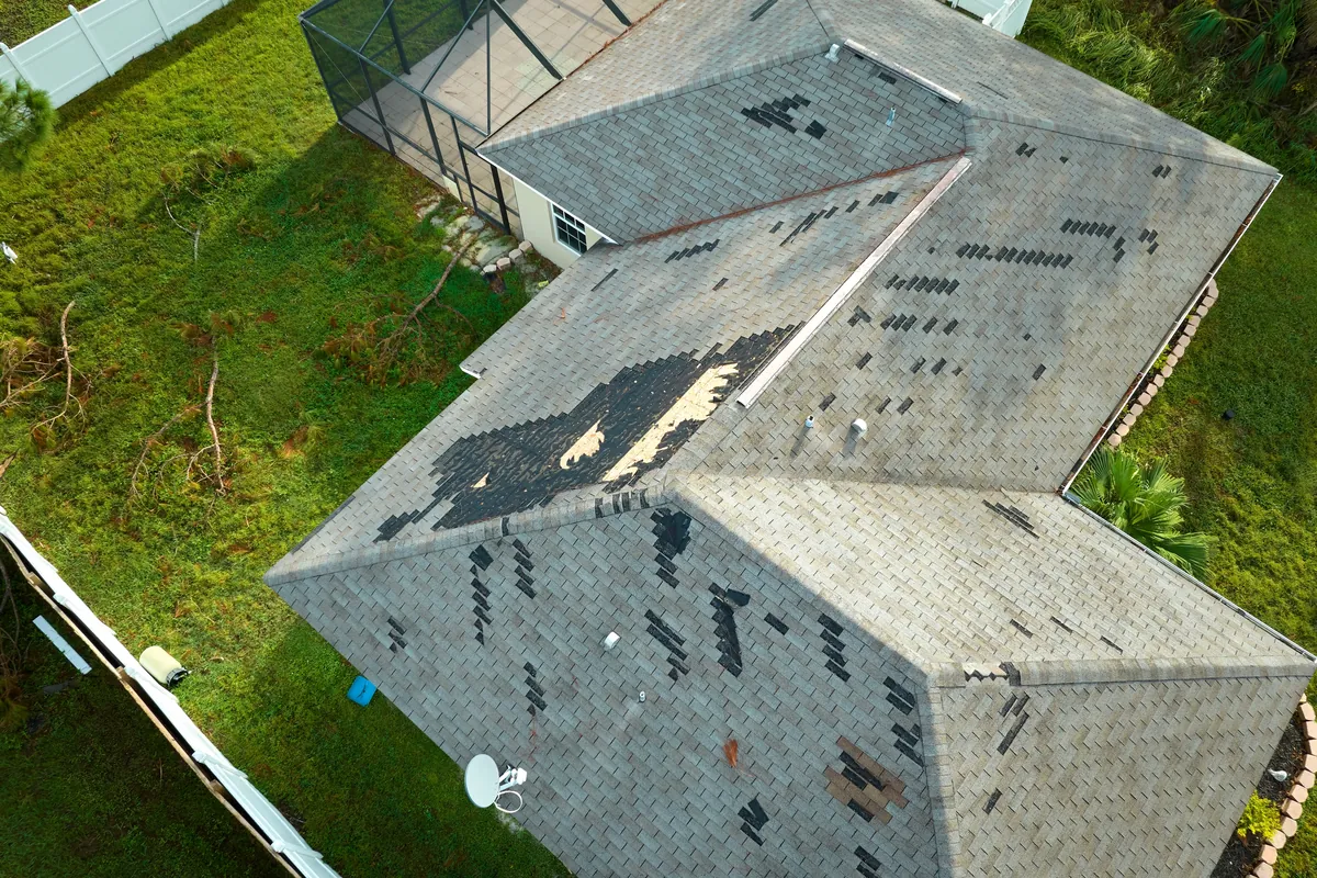 Aerial view of a shingle roof with missing and damaged shingles after a hurricane