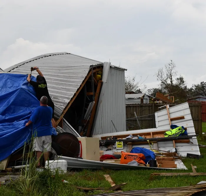 Two people tarping a storm-damaged metal building after a hurricane